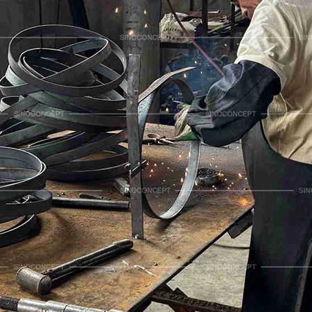 Worker welding steel rings for outdoor litter bins during frame fabrication in the factory