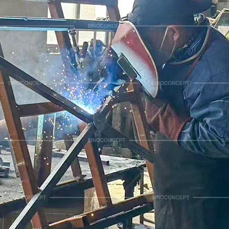 Worker welding mild steel pedestrian guardrails during frame assembly in factory