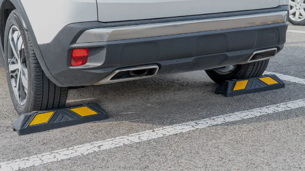 Black and yellow parking wheel stops positioned behind a car's rear tyres in an outdoor parking space